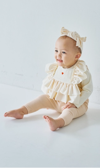 アイボリーのスタイとロンパスを着用したベビーモデルの画像